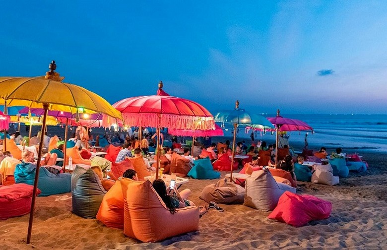 Bãi biển Seminyak lúc hoàng hôn, bóng người lướt sóng in trên nền trời cam đỏ