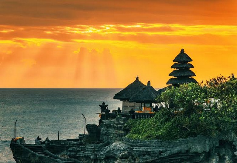 Cảnh hoàng hôn từ đền Tanah Lot với biển xanh và khách du lịch đứng ngắm từ xa