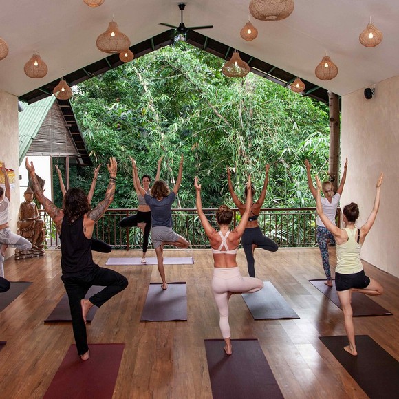 Không gian lớp học yoga ngoài trời tại The Yoga Barn Ubud với sàn gỗ và cây xanh bao quanh